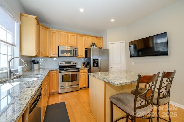 kitchen with a kitchen island, a breakfast bar, sink, light stone countertops, and appliances with stainless steel finishes