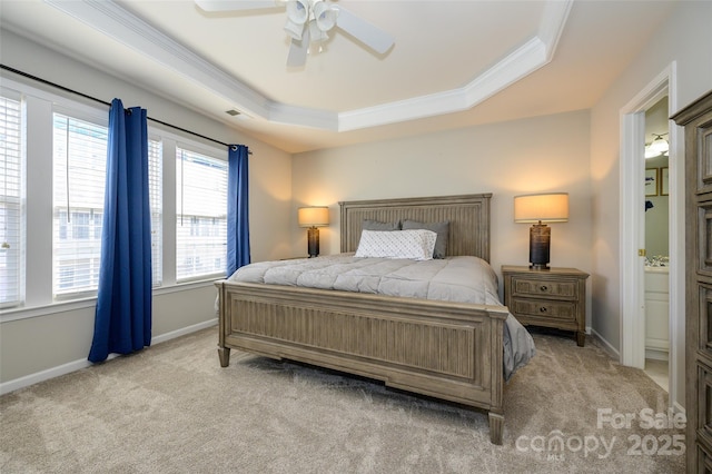 carpeted bedroom with ensuite bathroom, ceiling fan, ornamental molding, and a tray ceiling