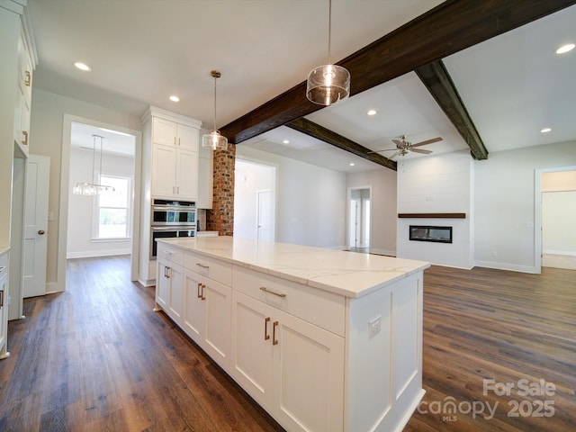 kitchen featuring a kitchen island, pendant lighting, white cabinets, light stone counters, and beamed ceiling