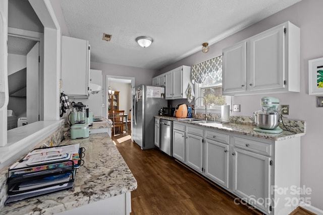 kitchen with sink, stainless steel appliances, a textured ceiling, white cabinets, and light stone counters