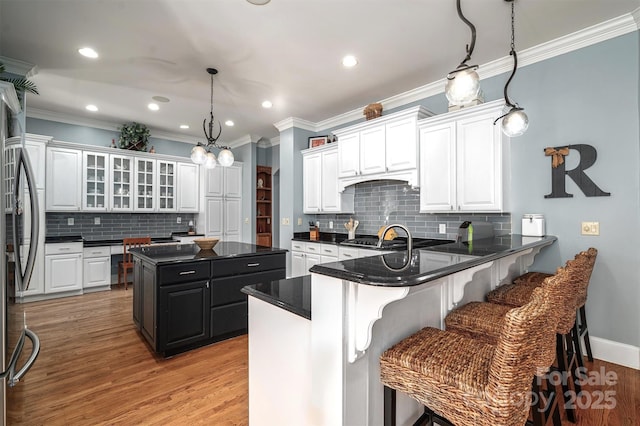 kitchen with decorative light fixtures, light hardwood / wood-style flooring, appliances with stainless steel finishes, a breakfast bar area, and white cabinets