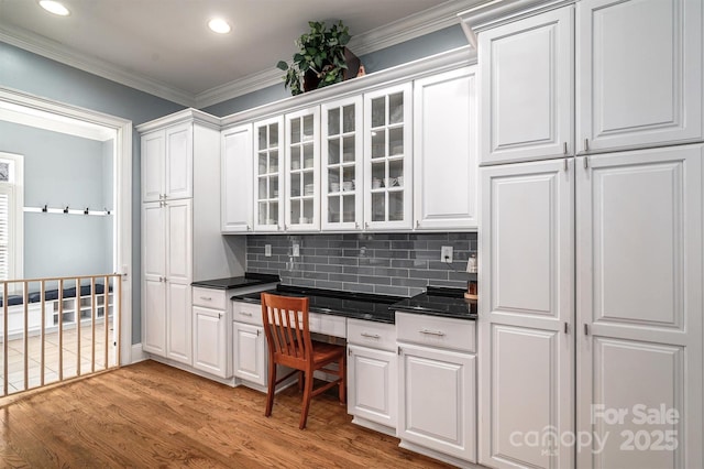 kitchen featuring built in desk, white cabinetry, decorative backsplash, light hardwood / wood-style floors, and crown molding