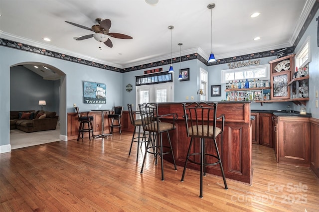 bar featuring ceiling fan, light wood-type flooring, crown molding, and pendant lighting