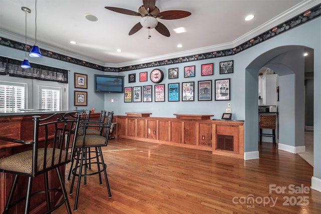 bar with hardwood / wood-style flooring, decorative light fixtures, ornamental molding, and ceiling fan