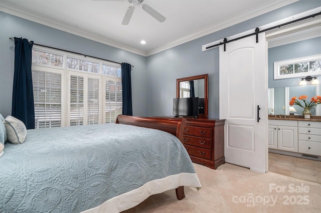 bedroom with light carpet, a barn door, ceiling fan, ensuite bath, and crown molding