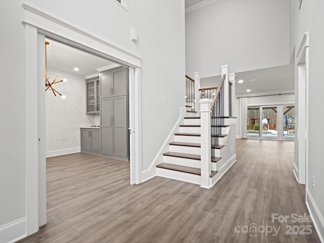 stairway with crown molding, hardwood / wood-style flooring, a chandelier, and a high ceiling