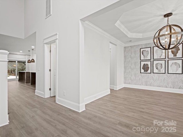 empty room featuring crown molding, a chandelier, light hardwood / wood-style floors, and a tray ceiling