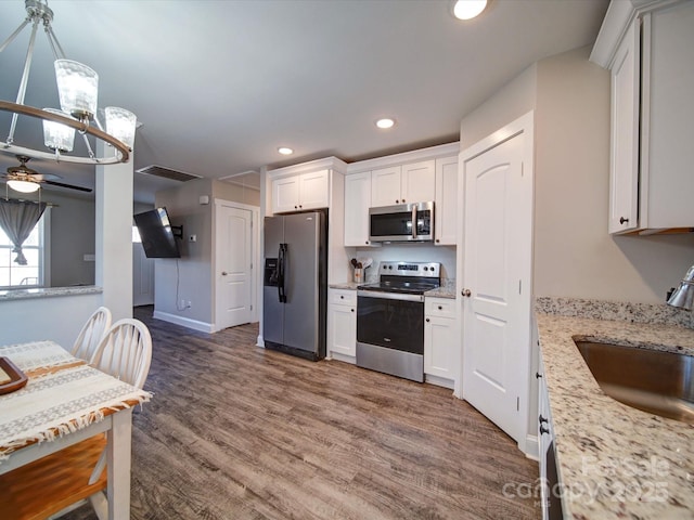 kitchen with light stone countertops, stainless steel appliances, white cabinetry, and sink