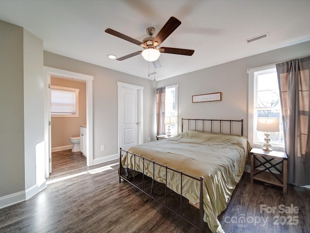 bedroom featuring ensuite bath, ceiling fan, dark hardwood / wood-style flooring, and multiple windows