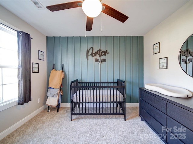 bedroom featuring light carpet, ceiling fan, and a nursery area