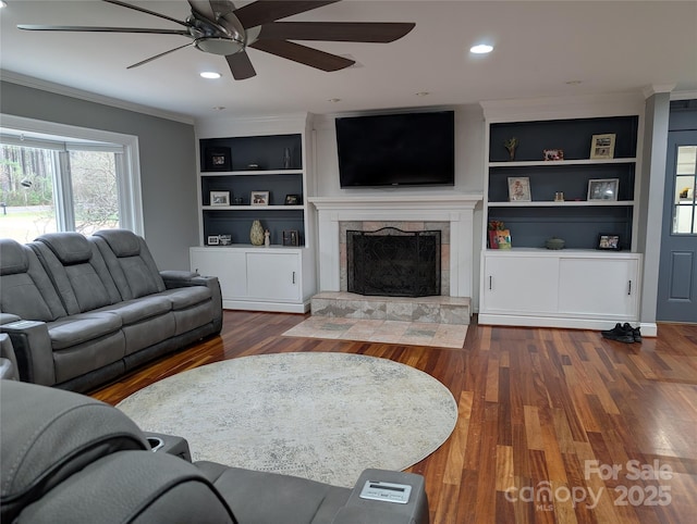 living room featuring ornamental molding, built in features, dark hardwood / wood-style flooring, and a stone fireplace