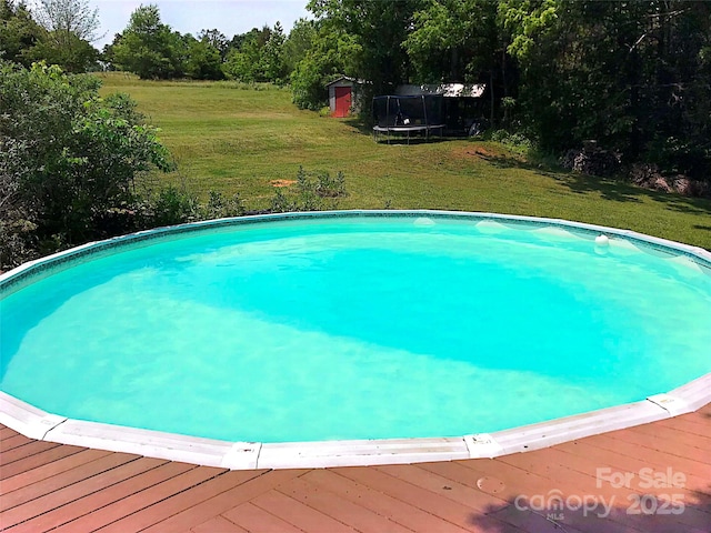 view of pool with a trampoline, a deck, a storage unit, and a yard