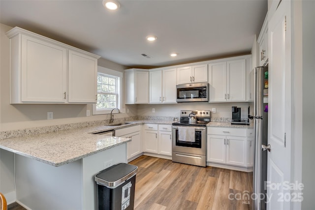 kitchen featuring kitchen peninsula, sink, white cabinetry, appliances with stainless steel finishes, and light stone counters