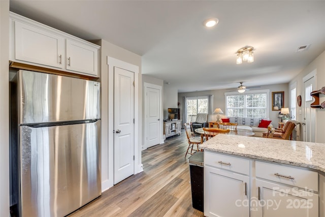 kitchen with light hardwood / wood-style floors, stainless steel fridge, ceiling fan, white cabinets, and light stone counters