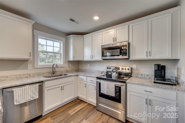 kitchen featuring white cabinets, appliances with stainless steel finishes, light hardwood / wood-style floors, sink, and light stone counters