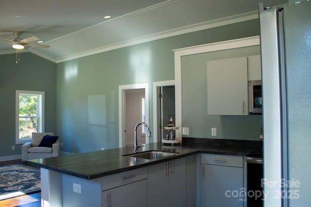 kitchen with white cabinetry, kitchen peninsula, stainless steel refrigerator, vaulted ceiling, and sink