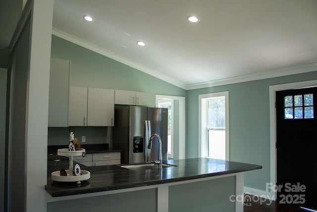 kitchen with lofted ceiling, kitchen peninsula, sink, crown molding, and stainless steel fridge with ice dispenser