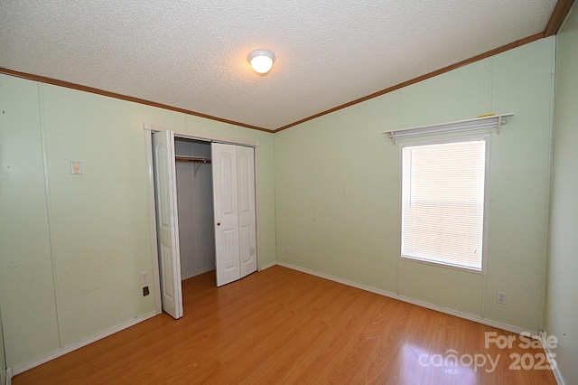 unfurnished bedroom featuring a closet, lofted ceiling, a textured ceiling, crown molding, and light hardwood / wood-style flooring