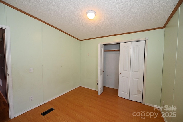 unfurnished bedroom with light hardwood / wood-style floors, a textured ceiling, a closet, and crown molding