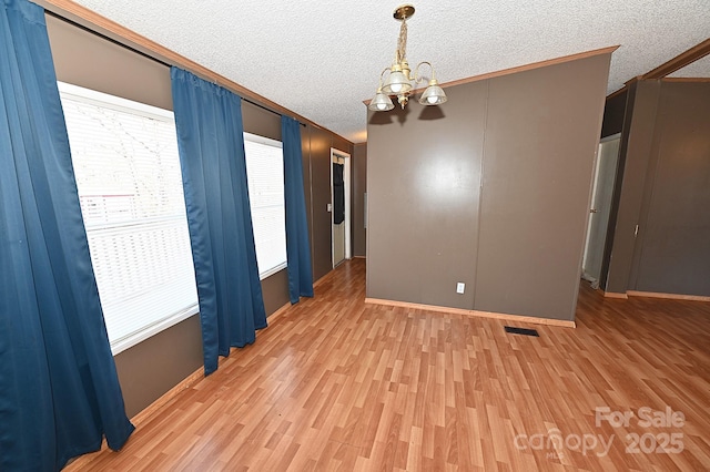 empty room featuring a textured ceiling, an inviting chandelier, crown molding, and hardwood / wood-style floors