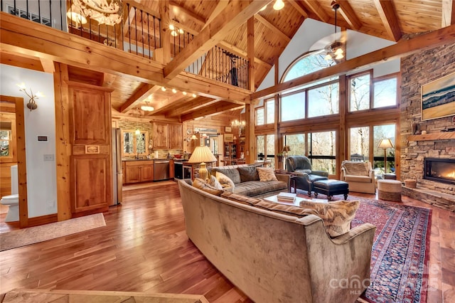 living room featuring high vaulted ceiling, plenty of natural light, light hardwood / wood-style flooring, and a stone fireplace