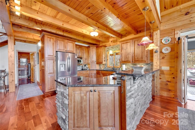 kitchen featuring kitchen peninsula, wood walls, stainless steel appliances, dark stone countertops, and pendant lighting