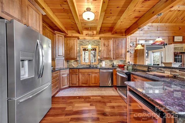 kitchen with appliances with stainless steel finishes, dark stone counters, pendant lighting, beam ceiling, and sink