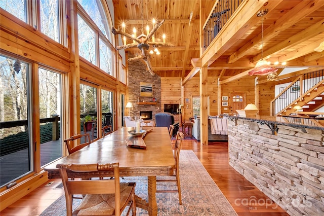 dining area featuring wood ceiling, hardwood / wood-style flooring, a notable chandelier, a towering ceiling, and a fireplace