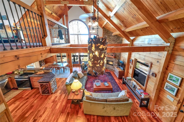 living room with hardwood / wood-style flooring, a stone fireplace, wooden ceiling, high vaulted ceiling, and beam ceiling