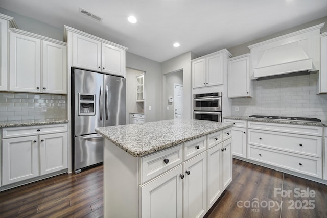 kitchen featuring tasteful backsplash, premium range hood, stainless steel appliances, and white cabinetry