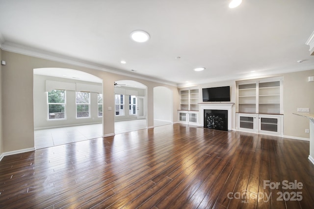 unfurnished living room with ceiling fan, ornamental molding, dark hardwood / wood-style floors, and built in shelves