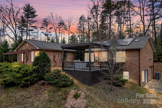 back house at dusk with a garage, a wooden deck, central AC, and solar panels