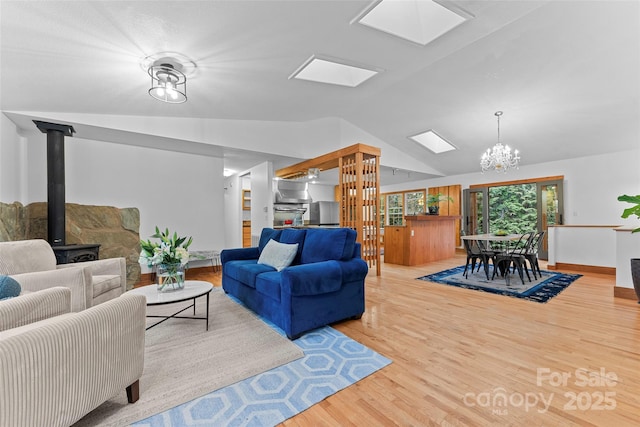 living room with an inviting chandelier, vaulted ceiling with skylight, light hardwood / wood-style floors, and a wood stove