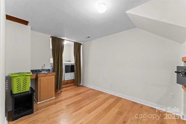 kitchen featuring lofted ceiling, sink, washer / dryer, and light hardwood / wood-style floors