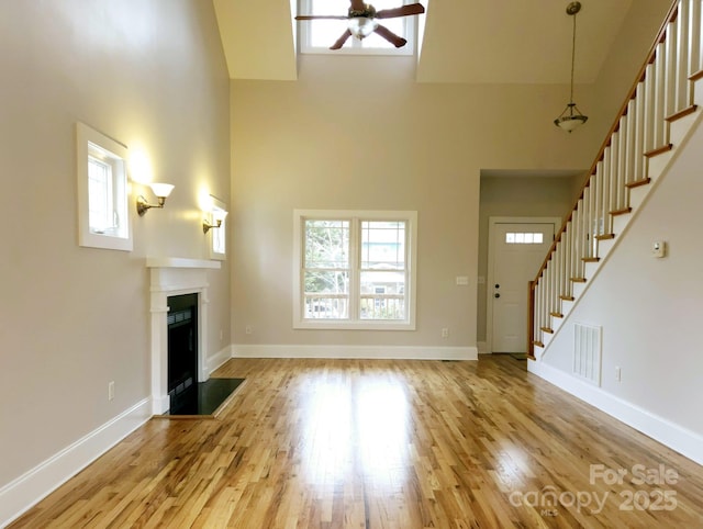 unfurnished living room featuring wood-type flooring, ceiling fan, and a high ceiling