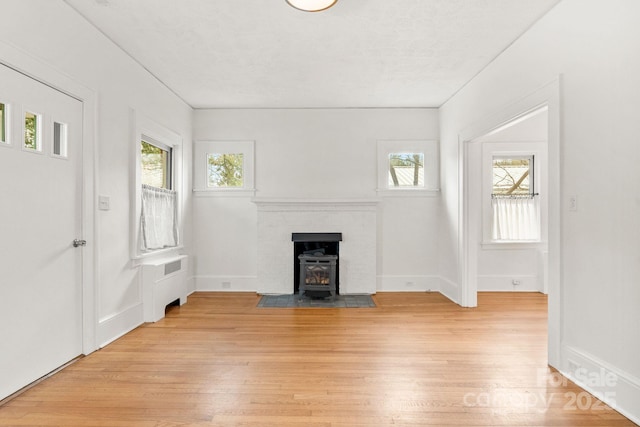 unfurnished living room featuring radiator heating unit, light hardwood / wood-style floors, a healthy amount of sunlight, and a wood stove