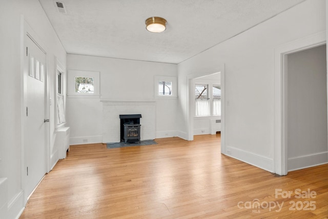 unfurnished living room featuring light hardwood / wood-style flooring, a wealth of natural light, and a wood stove