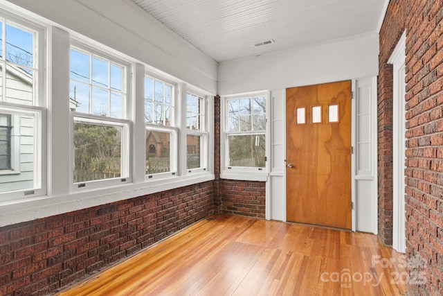 foyer entrance featuring hardwood / wood-style floors, plenty of natural light, and brick wall