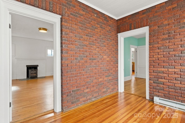 empty room with brick wall, a wood stove, hardwood / wood-style flooring, baseboard heating, and crown molding