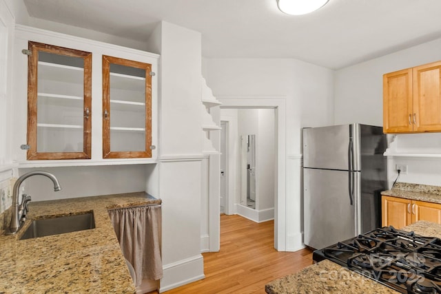 kitchen featuring stainless steel refrigerator, sink, light stone counters, and light hardwood / wood-style flooring