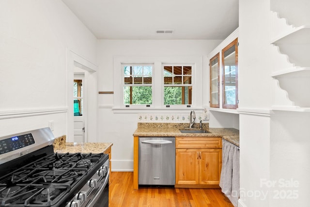 kitchen with light hardwood / wood-style floors, stainless steel appliances, light stone countertops, and sink