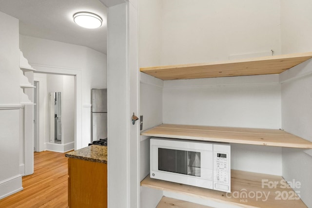 kitchen featuring light hardwood / wood-style flooring, built in desk, stainless steel refrigerator, and dark stone countertops