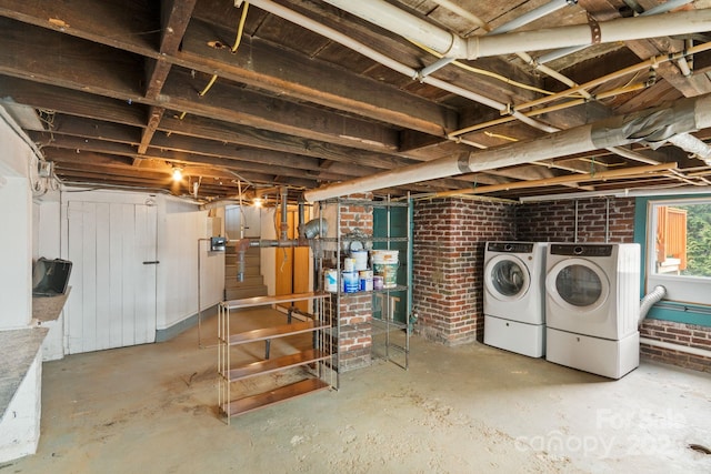 basement featuring washing machine and clothes dryer and brick wall