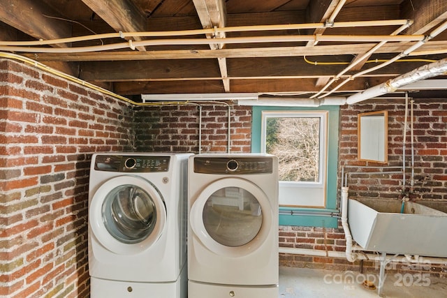 clothes washing area with brick wall, separate washer and dryer, and sink