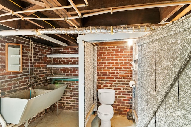 bathroom with sink, concrete floors, toilet, and brick wall