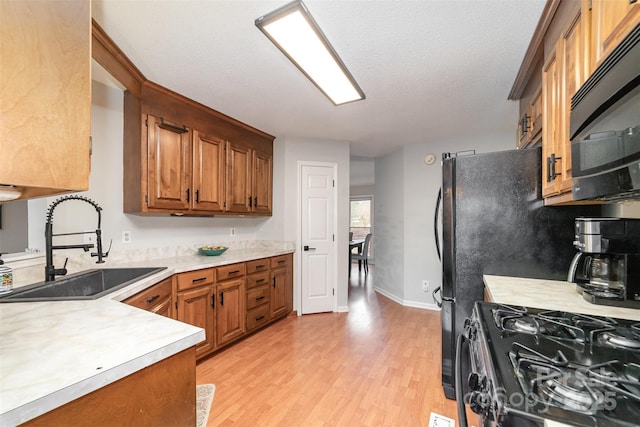 kitchen with sink, range with gas stovetop, a textured ceiling, and light wood-type flooring