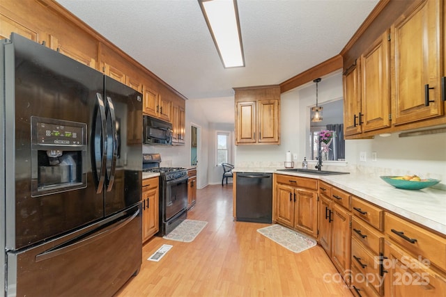 kitchen featuring sink, light hardwood / wood-style flooring, hanging light fixtures, black appliances, and a textured ceiling