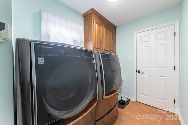 laundry room featuring cabinets, washing machine and clothes dryer, and light wood-type flooring