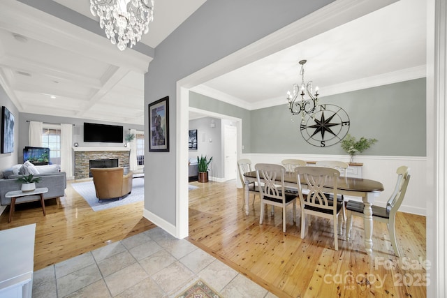 tiled dining area featuring crown molding, beam ceiling, a stone fireplace, coffered ceiling, and an inviting chandelier