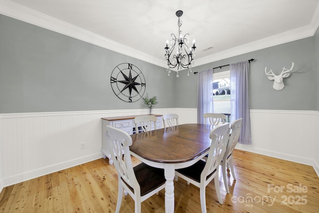 dining space with crown molding, light hardwood / wood-style floors, and an inviting chandelier